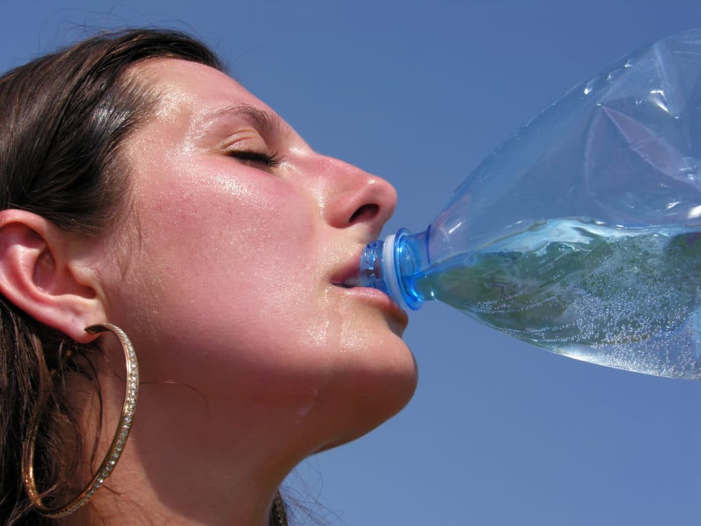 Überhitzte Frau trinkt Wasser aus der Flasche