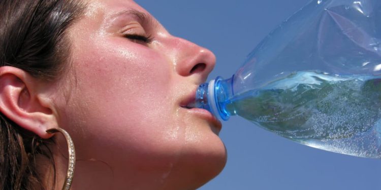 Überhitzte Frau trinkt Wasser aus der Flasche