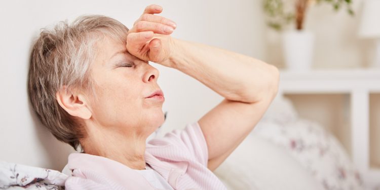 Eine erschöpfte ältere Frau fasst sich an die Stirn