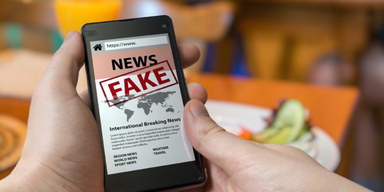 Eine Person hält ein Smartphone in der Hand, auf welchem ein als Fakenews gekennzeichneter Artikel zu sehen ist.