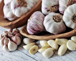 Knoblauchknollen und Knoblauchzehen auf einem weißen Tisch und in Holzschalen