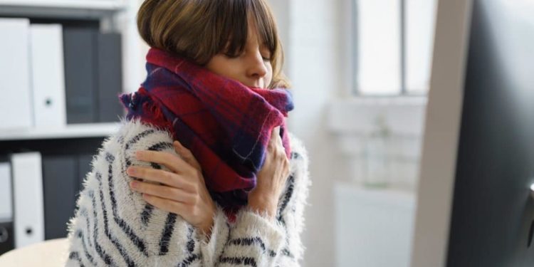 Eine erkältete Frau wärmt sich mit einem Schal und ihren Händen