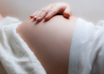 Eine schwangere Frau liegt auf dem Rücken und hält sich die rechte Hand auf den Bauch