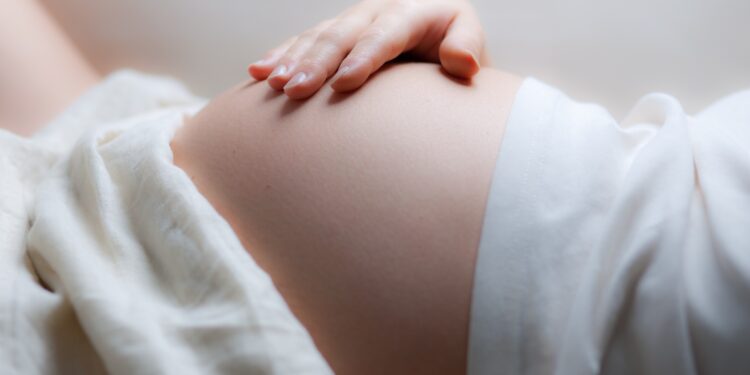Eine schwangere Frau liegt auf dem Rücken und hält sich die rechte Hand auf den Bauch