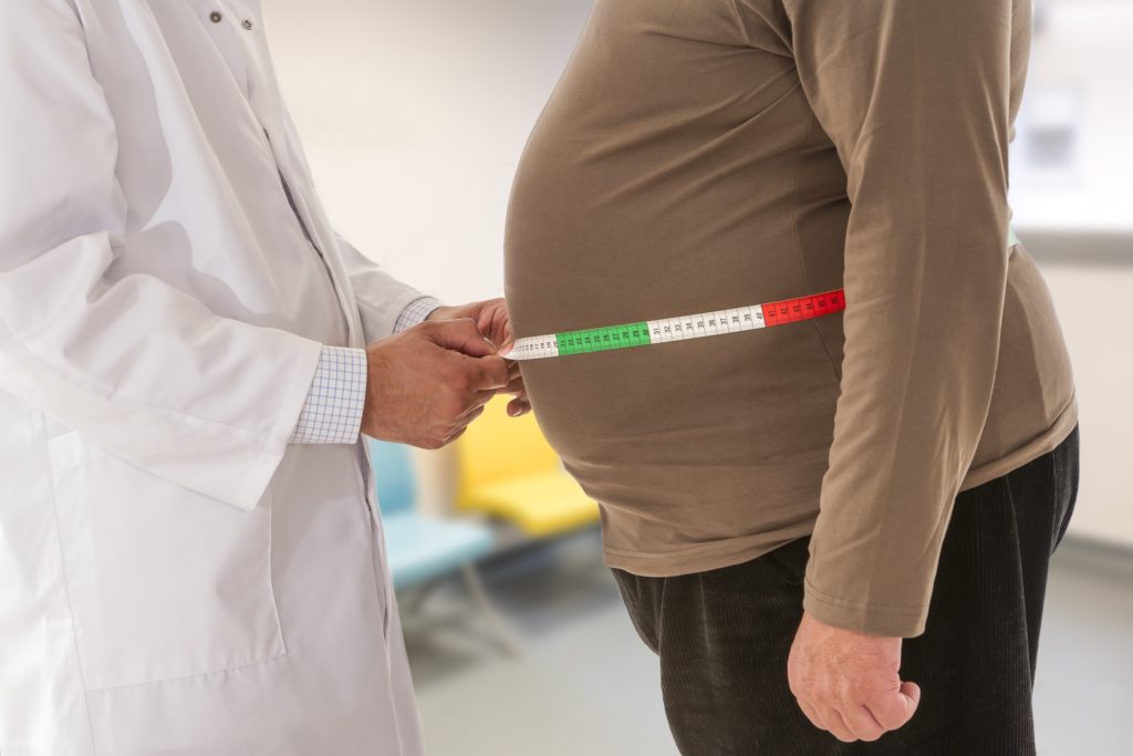 Arzt misst bei einem übergewichtigen Mann den Bauchumfang