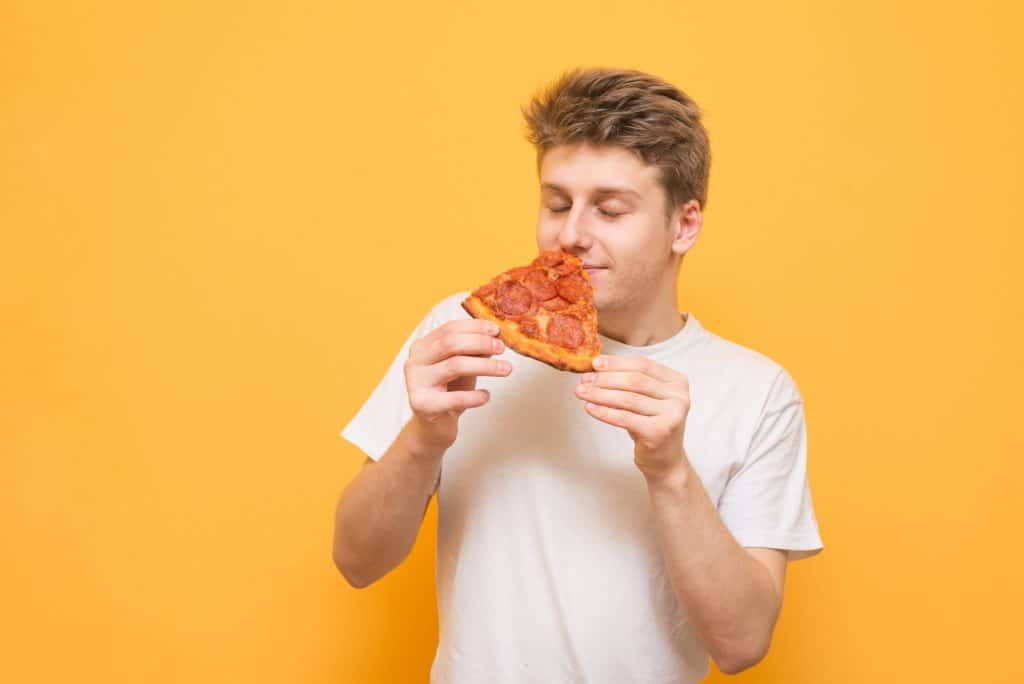 Junger Mann riecht an einem Stück Pizza