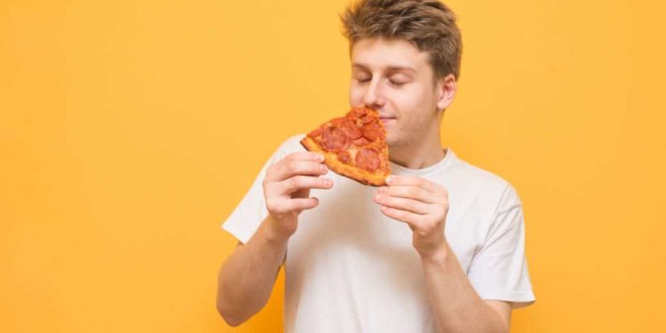 Junger Mann riecht an einem Stück Pizza