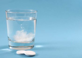 Zwei Brausetabletten liegen vor einem Glas Wasser.