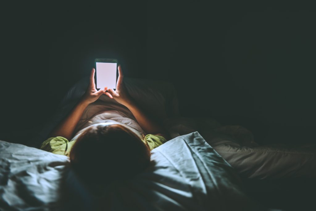 Junge Frau liegt nachts mit Smartphone im Bett
