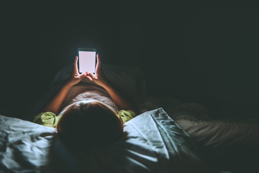 Young woman lying at night with smartphone in bed