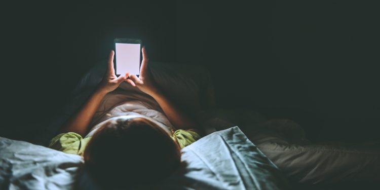 Junge Frau liegt nachts mit Smartphone im Bett