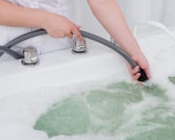 Eine Badewanne mit sprudelndem Wasser in das eine Frau einen Schlauch steckt