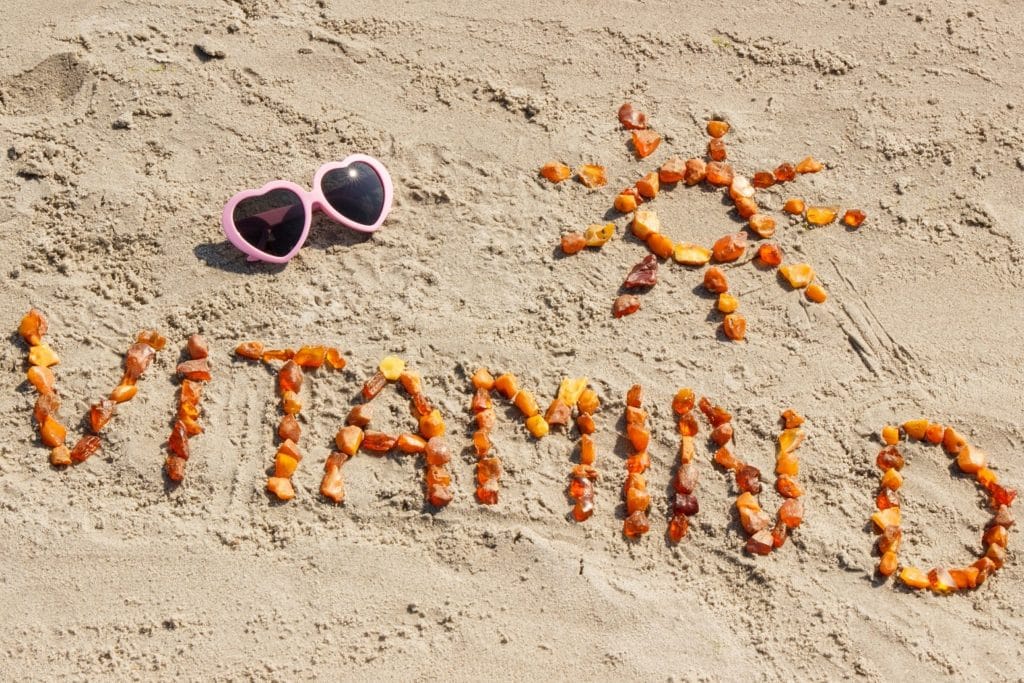 Sonnenbrille und das aus kleinen Teilen zusammengesetzte Wort Vitamin D sowie die Form einer Sonne am Strand