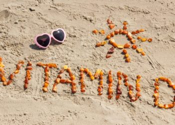 Sonnenbrille und das aus kleinen Teilen zusammengesetzte Wort Vitamin D sowie die Form einer Sonne am Strand