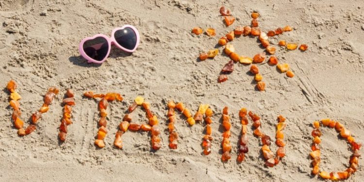 Sonnenbrille und das aus kleinen Teilen zusammengesetzte Wort Vitamin D sowie die Form einer Sonne am Strand