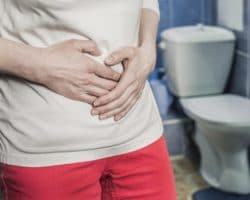 Ein Mann steht im Badezimmer vor der Toilette und fasst sich an den Bauch
