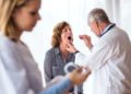 Ein älterer Arzt untersucht den Mundraum einer Patientin
