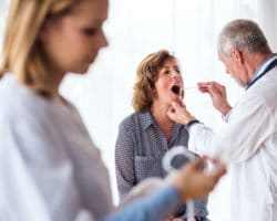 Ein älterer Arzt untersucht den Mundraum einer Patientin