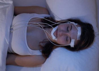 Eine schlafende Frau liegt in einem Bett und ist mit Elektroden verkabelt.