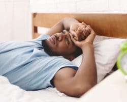 Junger Mann liegt mit geöffneten Augen schlaflos im Bett