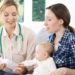 Gesundheitsschwester gibt Mutter mit Baby auf dem Schoß Ratschläge