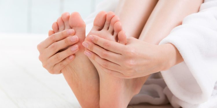 Füße einer Frau, die im Bademantel auf dem Boden sitzt und Ihre Fußsohlen anfässt