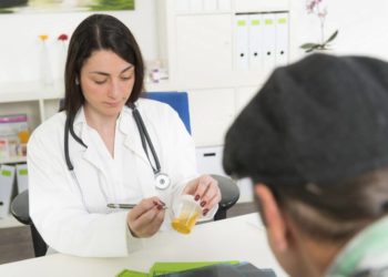 Ärztin nimmt Urinbecher entgegen und beschriftet diesen