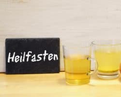 2 gefüllte Gläser, ein Apfel und eine Schiefertafel mit der Aufschrift "Heilfasten"