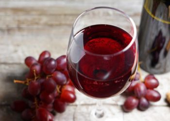 Rote Trauben und ein Glas Rotwein auf einem Holztisch