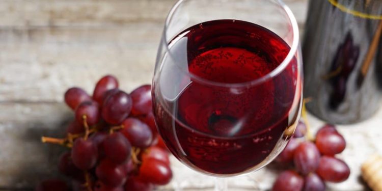 Rote Trauben und ein Glas Rotwein auf einem Holztisch