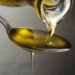 Olivenöl läuft aus einer Glasflasche auf einen Teelöffel