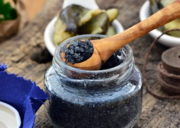 Holzlöffel hebt schwarzes Salz aus Glas