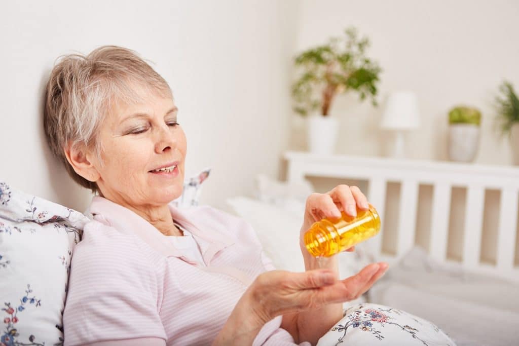 Ältere Frau sitzt auf Bett und kippt Medikamente auf Ihre Hand