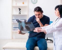 Ärztin zeigt einem hustenden Patienten eine Röntgenaufnahme