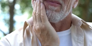 Mann fasst sich an die schmerzende Wange