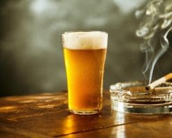 Volles Glas Bier und und brennende Zigaretten im Aschenbecher