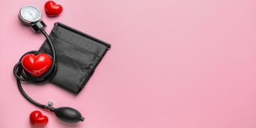 Blutdruckmessgerät mit roten Herzen vor rosa Hintergund.