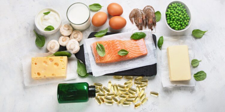 Vitamin-D-haltige Nahrungsmittel wie Lachs, Butter, Erbsen, Käse und Eier sowie ein Fläschchen mit ausgekippten Kapseln eines Nahrungsergänzungsmittels vor weißem Hintergrund