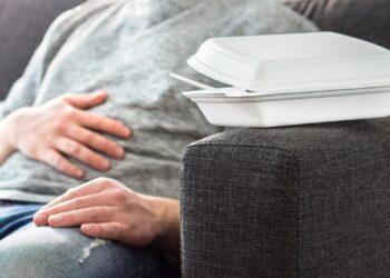 Ein Mann sitzt auf einem Sofa und hält sich eine Hand auf den Bauch.