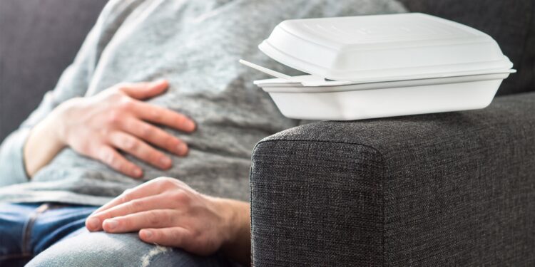 Ein Mann sitzt auf einem Sofa und hält sich eine Hand auf den Bauch.