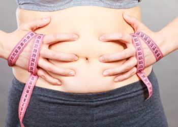 Frau mit einem Maßband berührt ihren Bauch