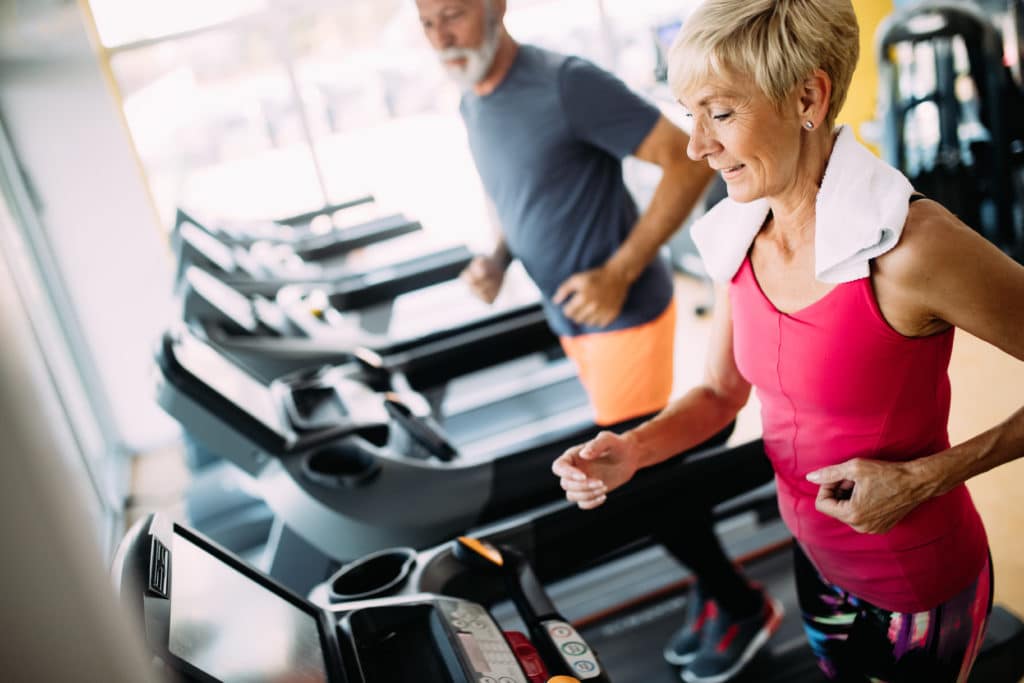 Zwei ältere Menschen laufen auf einem Laufband im Fitnesscenter