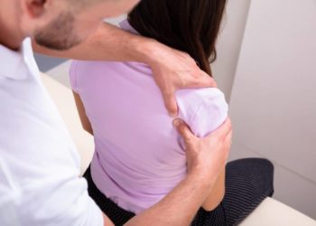 Behandler drückt mit den Daumen einen Punkt in Schulternähe der Patientin.