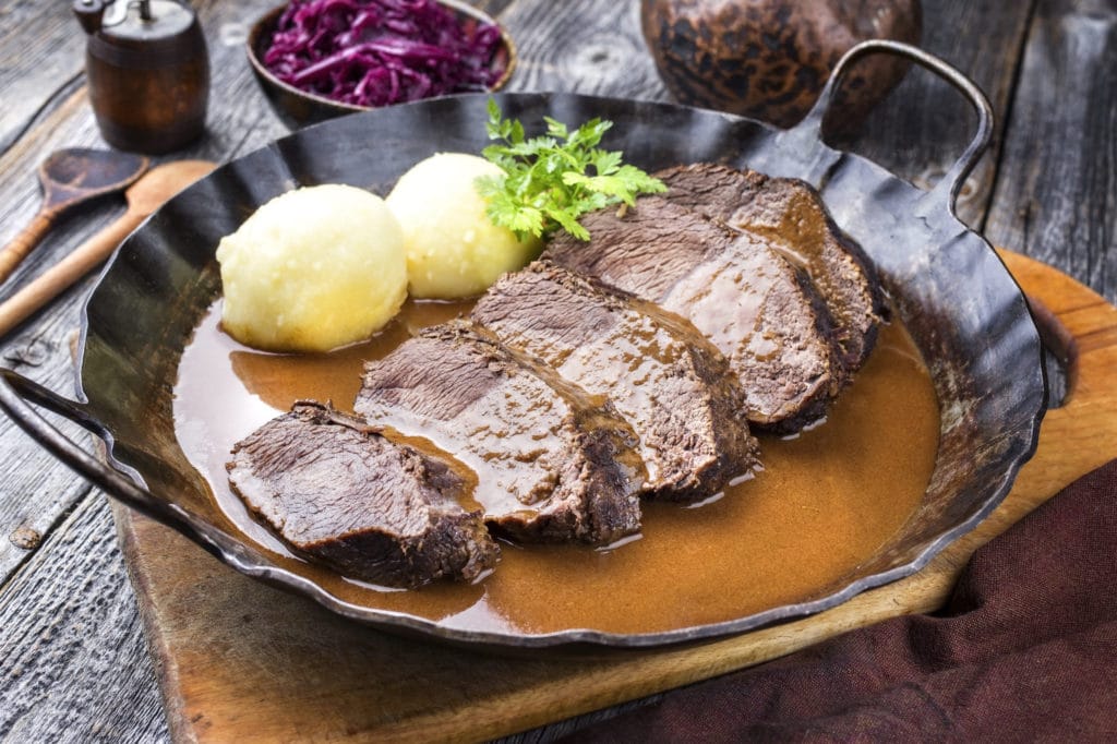 Sauerbraten und Kartoffelknödel in einer Pfanne mit Sauce