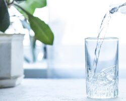Aus einer gläsernen Wasserkaraffe fließt klares Wasser in ein Glas