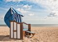 Blau und weiß gestreifter Strandkorb im Sand vor einer Kulisse von Meer und Himmel