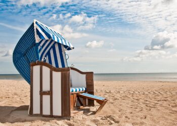 Blau und weiß gestreifter Strandkorb im Sand vor einer Kulisse von Meer und Himmel