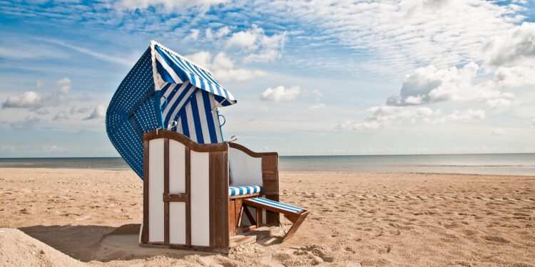 Blau und weiß gestreifter Strandkorb im Sand vor einer Kulisse von Meer und Himmel