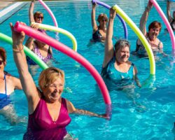 Gruppe fröhlicher Seniorinnen bei der Wassergymnastik mit Poolnudeln