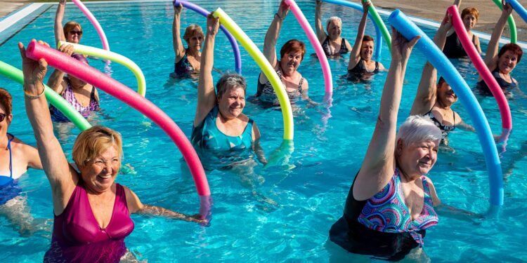 Gruppe fröhlicher Seniorinnen bei der Wassergymnastik mit Poolnudeln